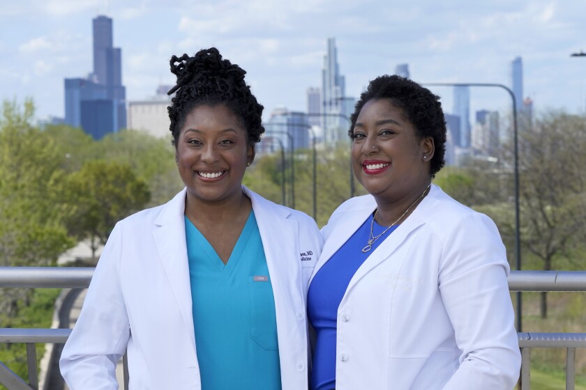 Dr. Brittani James, left, and her twin sister Dr. Brandi Jackson stand for a portrait in the Bronzeville neighborhood of Chicago, Sunday, May 2, 2021. The identical twin doctors who have fought bigotry all their lives have a lofty new mission: dismantling racism in medicine. (AP Photo/Charles Rex Arbogast)