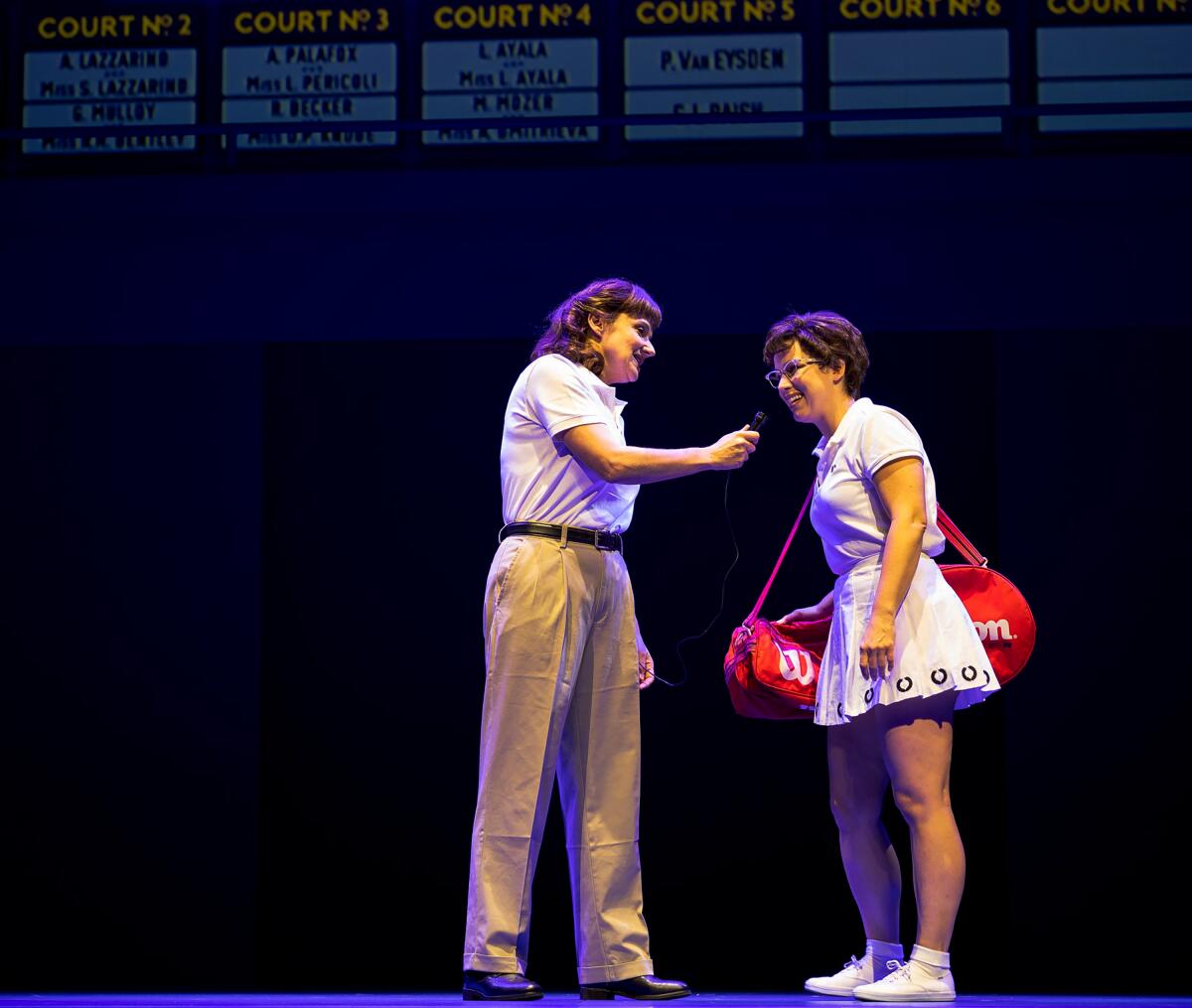 An actor in khakis and a white polo stands next to another dressed up as Billie Jean King in a scene from "Love All"