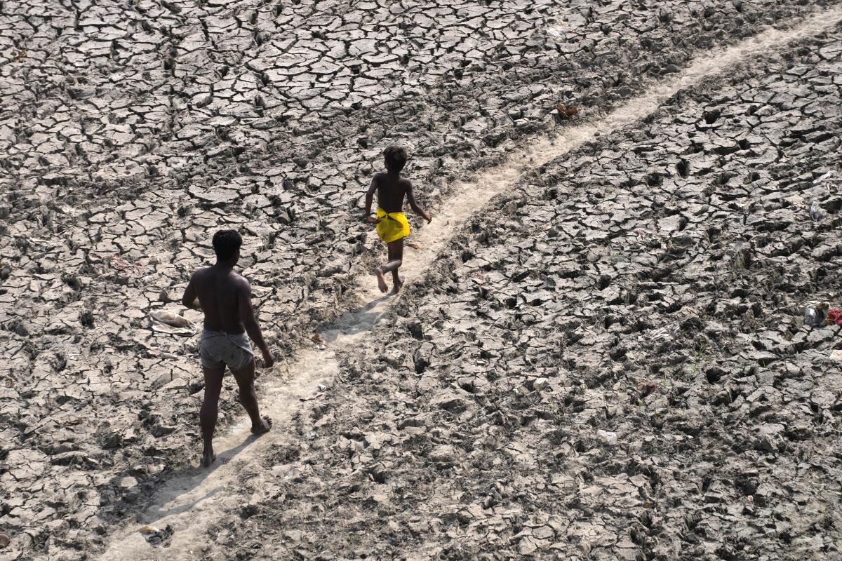 A man and a boy walk across a dry riverbed.