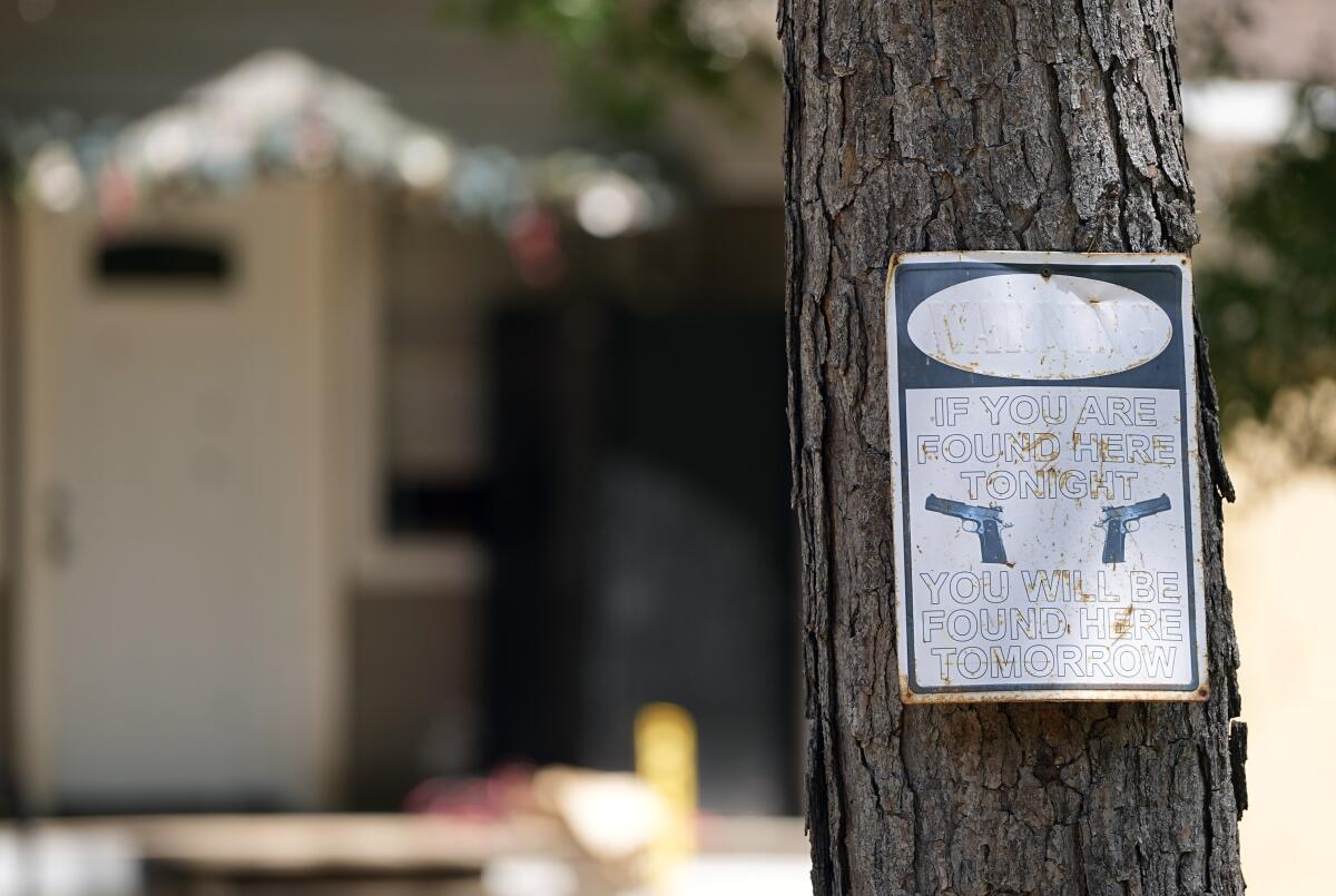 A sign on a tree shows handguns and says, "If you are found here tonight, you will be found here tomorrow."