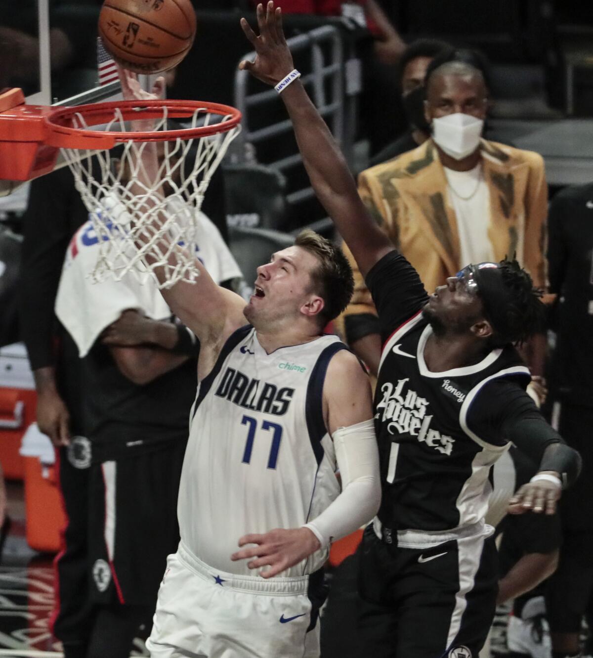 Mavericks guard Luka Doncic #77 lays in an alley-oop while defended by Clippers guard Reggie Jackson.