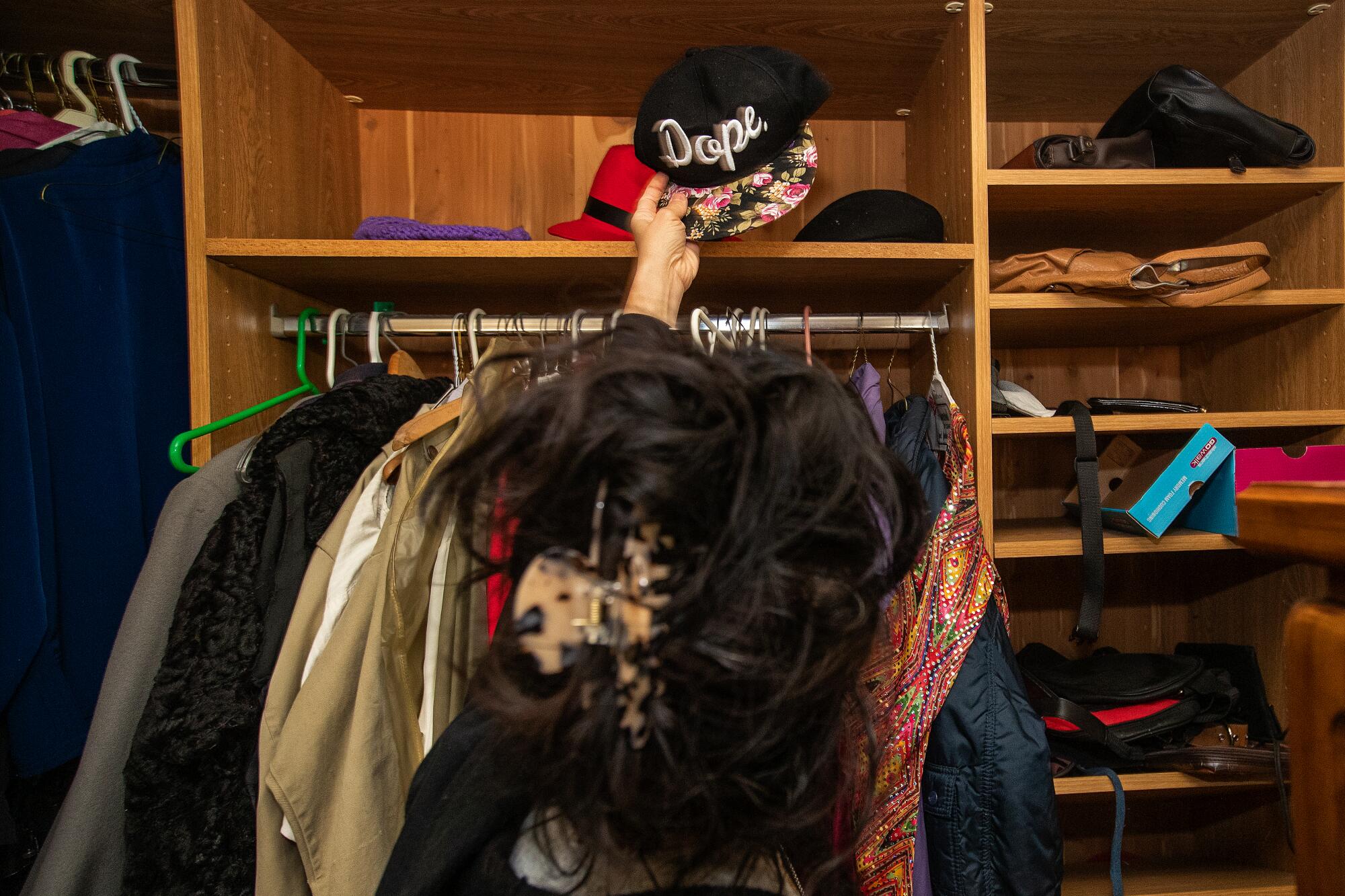 A woman grabbing a baseball cap that reads, "dope" off a high shelf.