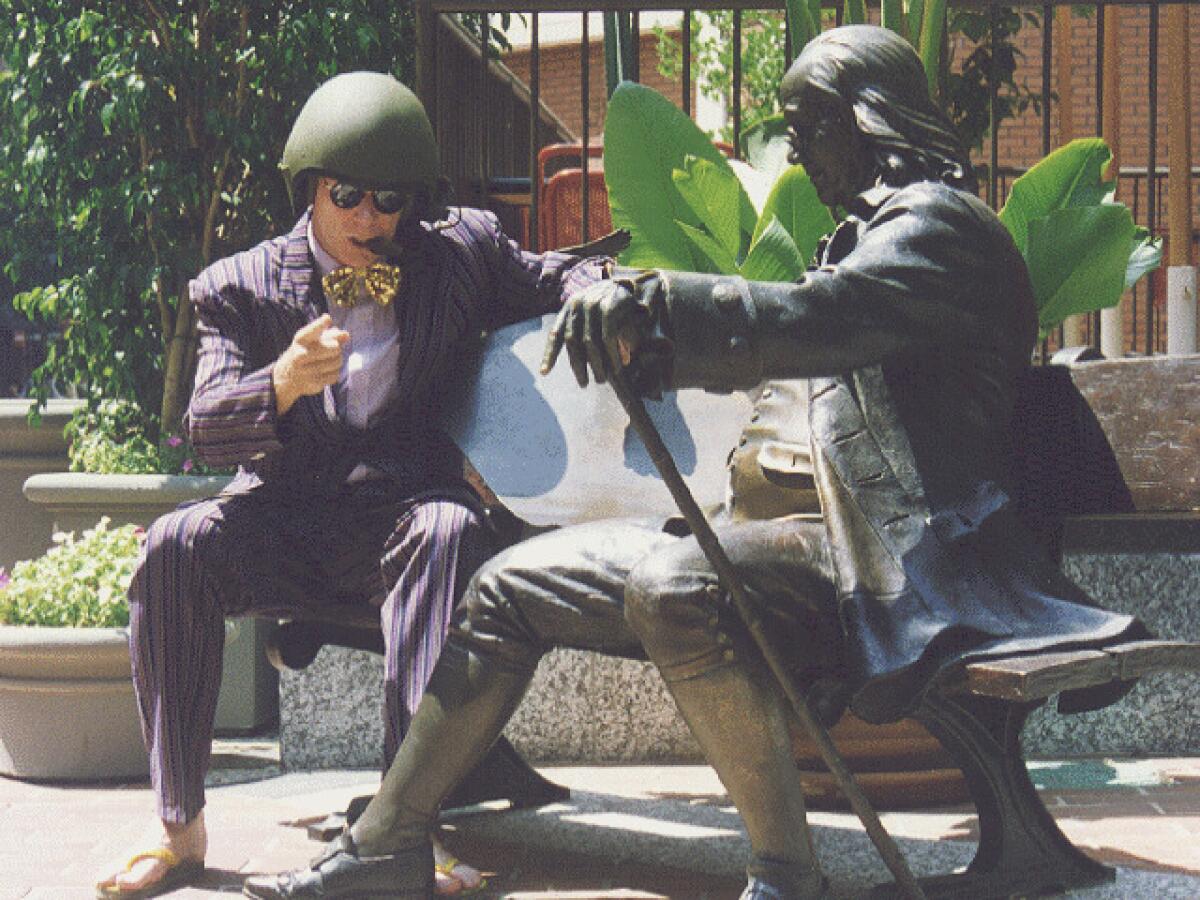 An actor in a helmet sits by a statue in "Plumbers Don't Wear Ties."