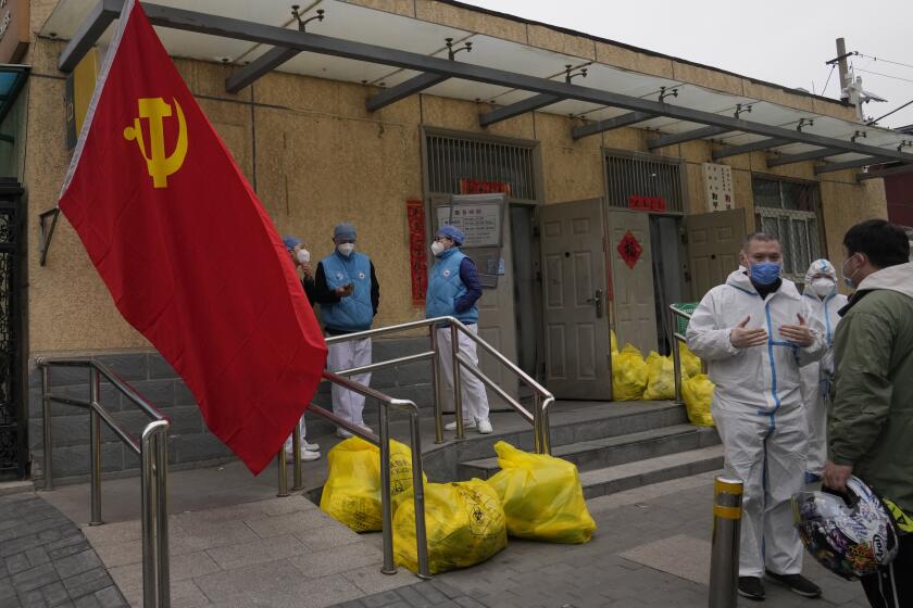 Community workers outside a locked down community chat near a Communist Party flag and trash bags labelled as hazardous waste on Thursday, March 17, 2022, in Beijing. Even as authorities lock down cities in China's worst outbreak in two years, they are looking for an exit ramp from what has been a successful but onerous COVID-19 prevention strategy. (AP Photo/Ng Han Guan)