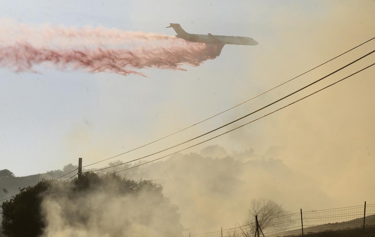 A plane drops fire retardant on a fire along Highway 68 east of Laureles Grade in rural Salinas, Calif., on Saturday, Sept. 19, 2015.