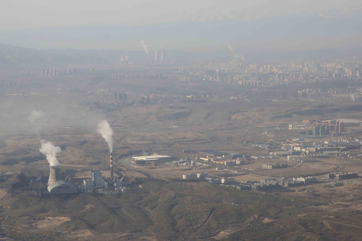 An aerial view of a hazy sky shows smoke rising from smokestacks.