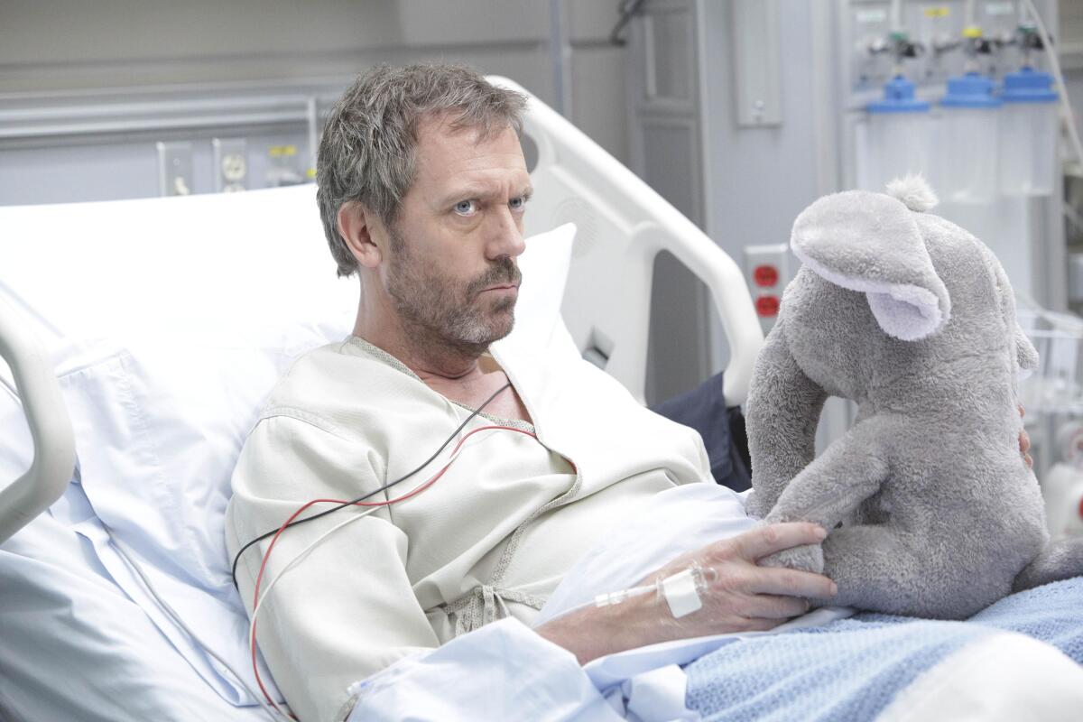 A grumpy man in a hospital bed holds a stuffed elephant.