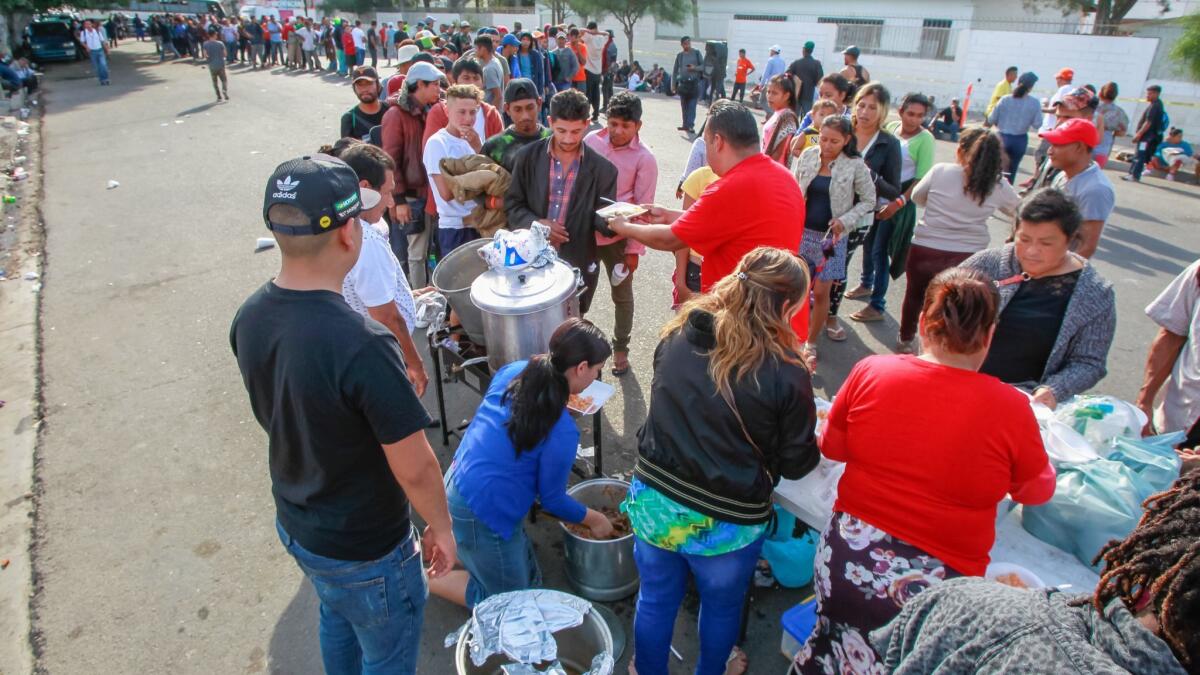 Migrants line up for food served by members of a Tijuana church called Tabernaculo de Adoration Familiar outside the temporary shelter at Unidad Deportiva Benito Juarez in Tijuana, Mexico