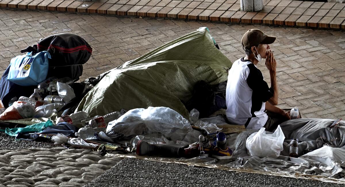 A man smokes on a sidewalk with his possessions huddled nearby
