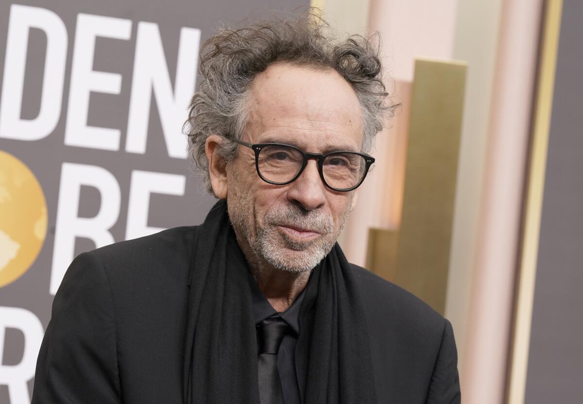 Tim Burton wears an all-black suit and scarf as he poses for photos at a red carpet event