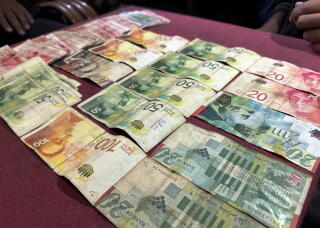 Israeli shekel notes are laid out on a table in a cafe.