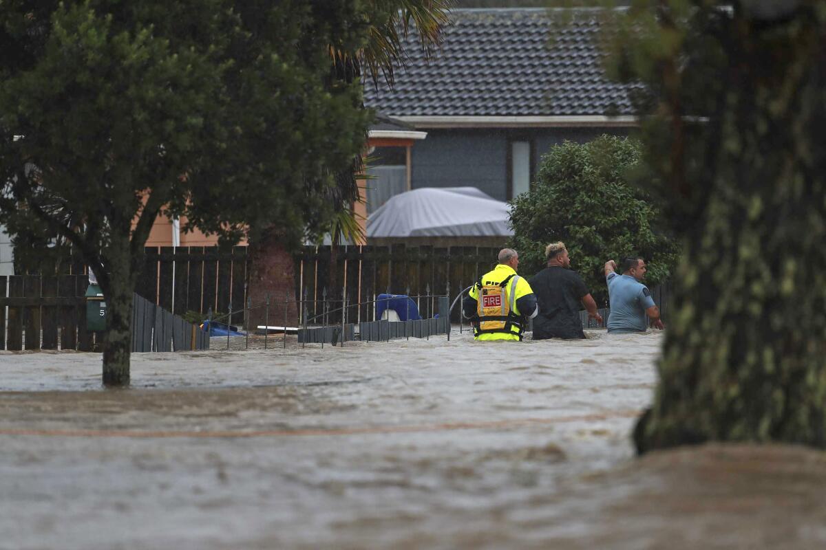 Emergency workers and a man wade through flood waters.