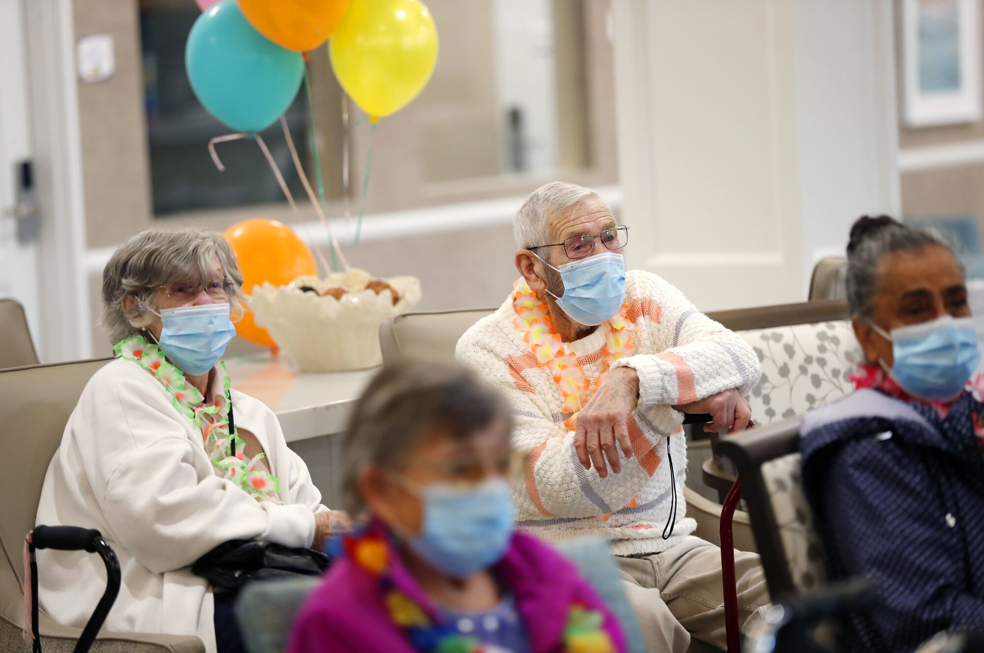 four older adults sit watching a program wearing masks. 