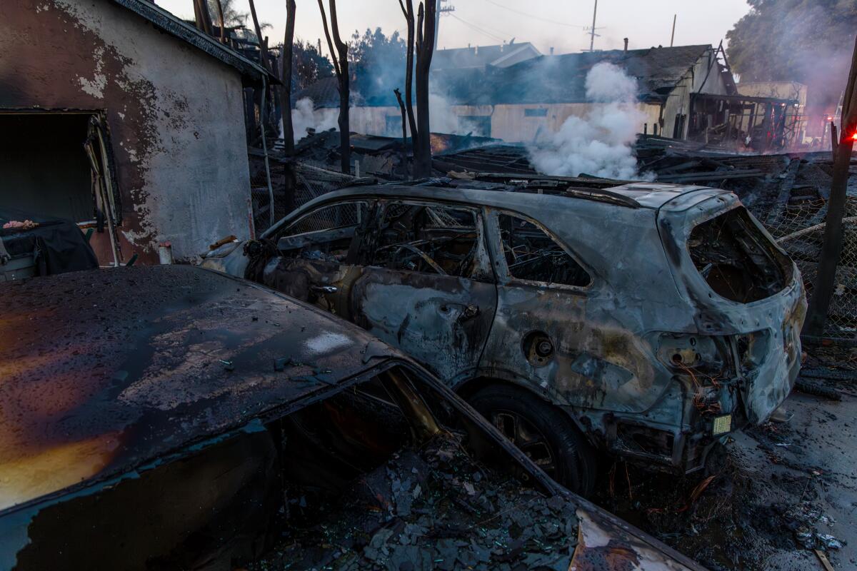 Blackened, burned-out cars smoldering outside a destroyed home