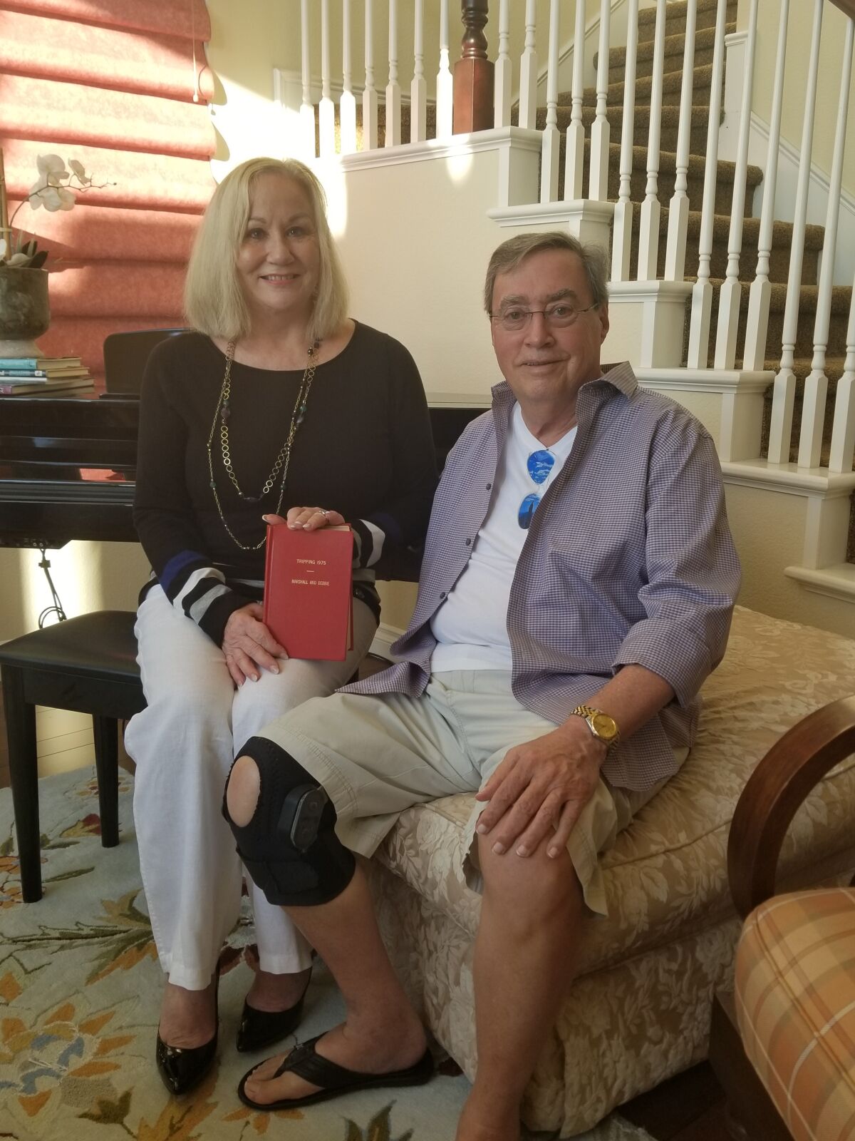 Debbie and Marshall Hockett in their living room in Encinitas, with their original travel journal.