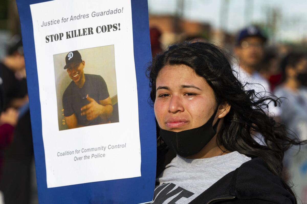 A woman holds up a poster with a photo of Andres Guardado that says "Stop killer cops!"