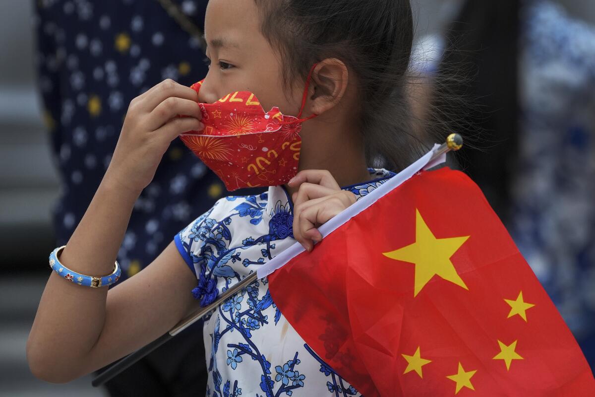 A child holds a national flag while adjusting her face mask on a street in Beijing, Tuesday, Aug. 9, 2022. Chinese authorities have closed Tibet's famed Potala Palace after a minor outbreak of COVID-19 was reported in the Himalayan region. (AP Photo/Andy Wong)