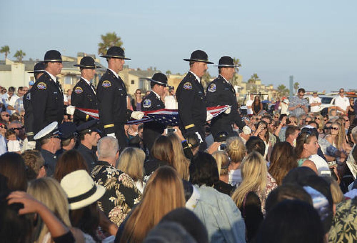 Members of the Huntington Beach and Costa Mesa Fire Honor Guard carry the flag to the stage to close the Ben Carlson Celebration of Life ceremony on the beach at Orange Street in Newport Beach on Sunday evening.