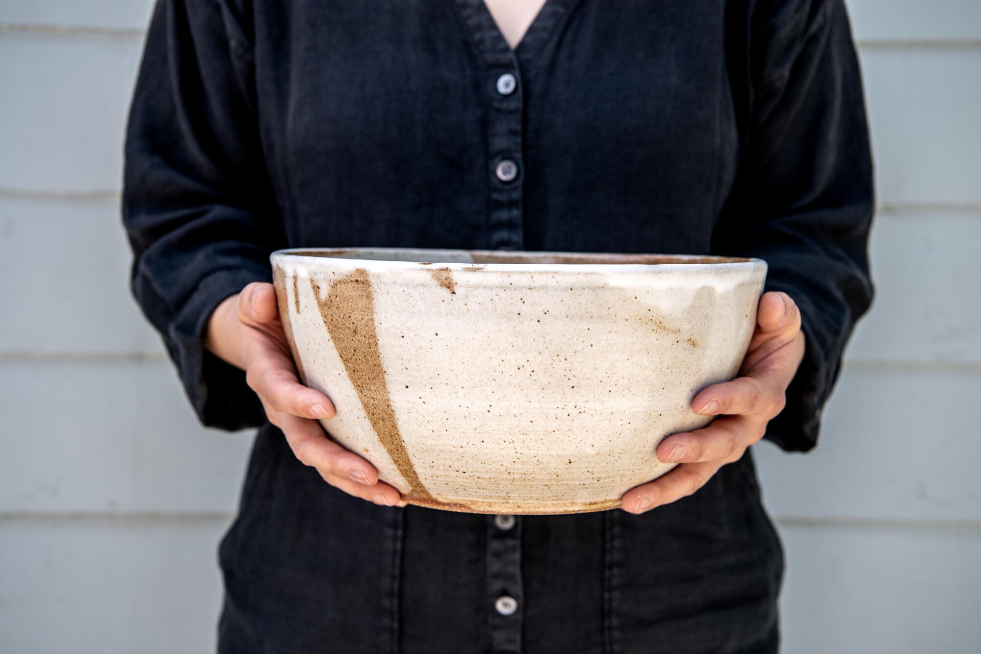 A close-up on the hands of a woman standing holding a large clay bowl.