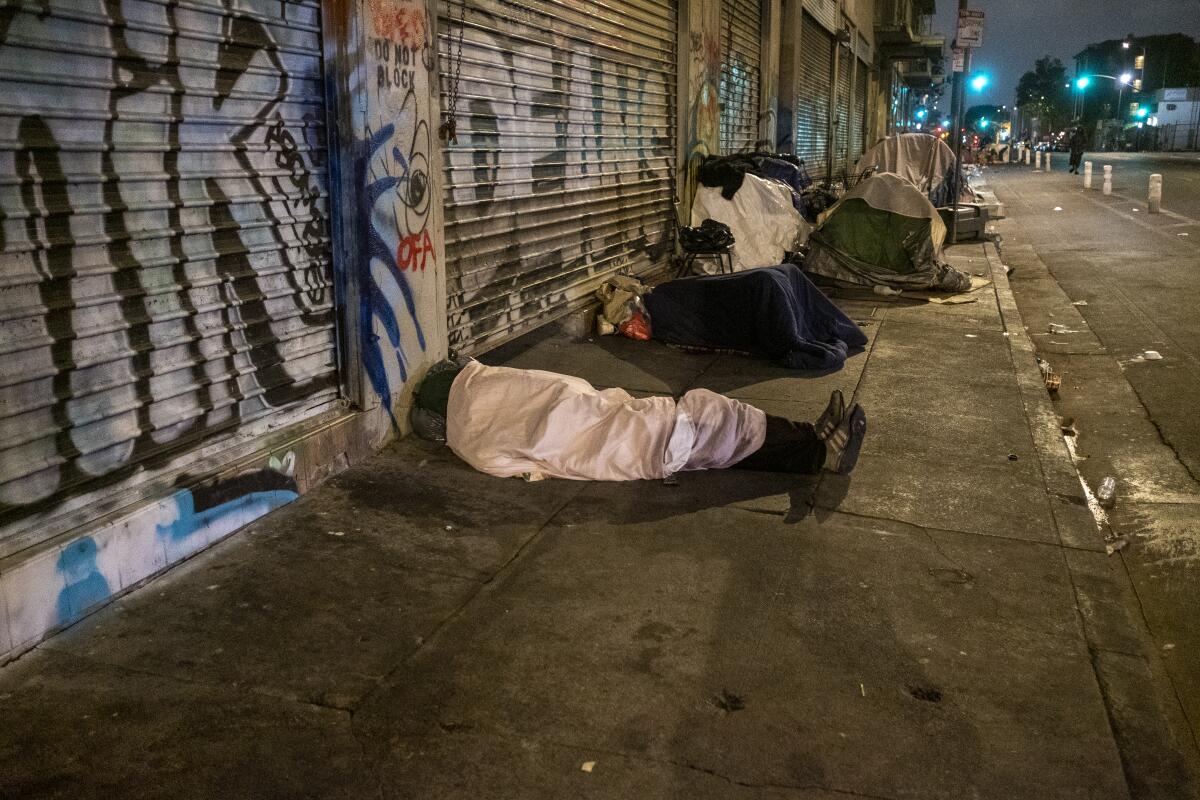 People sleep under blankets and inside tents on a skid row sidewalk 