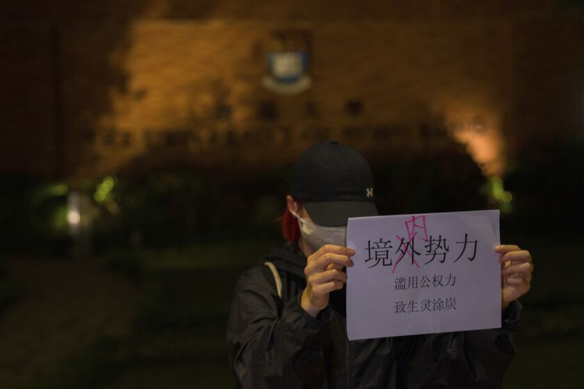 A protester holds up a paper which reads "Not foreign forces but internal forcers" and "Abuse of Government power plunge the people into misery and suffering" during a gathering at the University of Hong Kong in Hong Kong, Tuesday, Nov. 29, 2022. On Tuesday, about a dozen people gathered at the University of Hong Kong, chanting against virus restrictions and holding up sheets of paper with critical slogans. Most were from the mainland, which has a separate legal system from the Chinese territory of Hong Kong, and some spectators joined in their chants. (AP Photo/Bertha Wang)