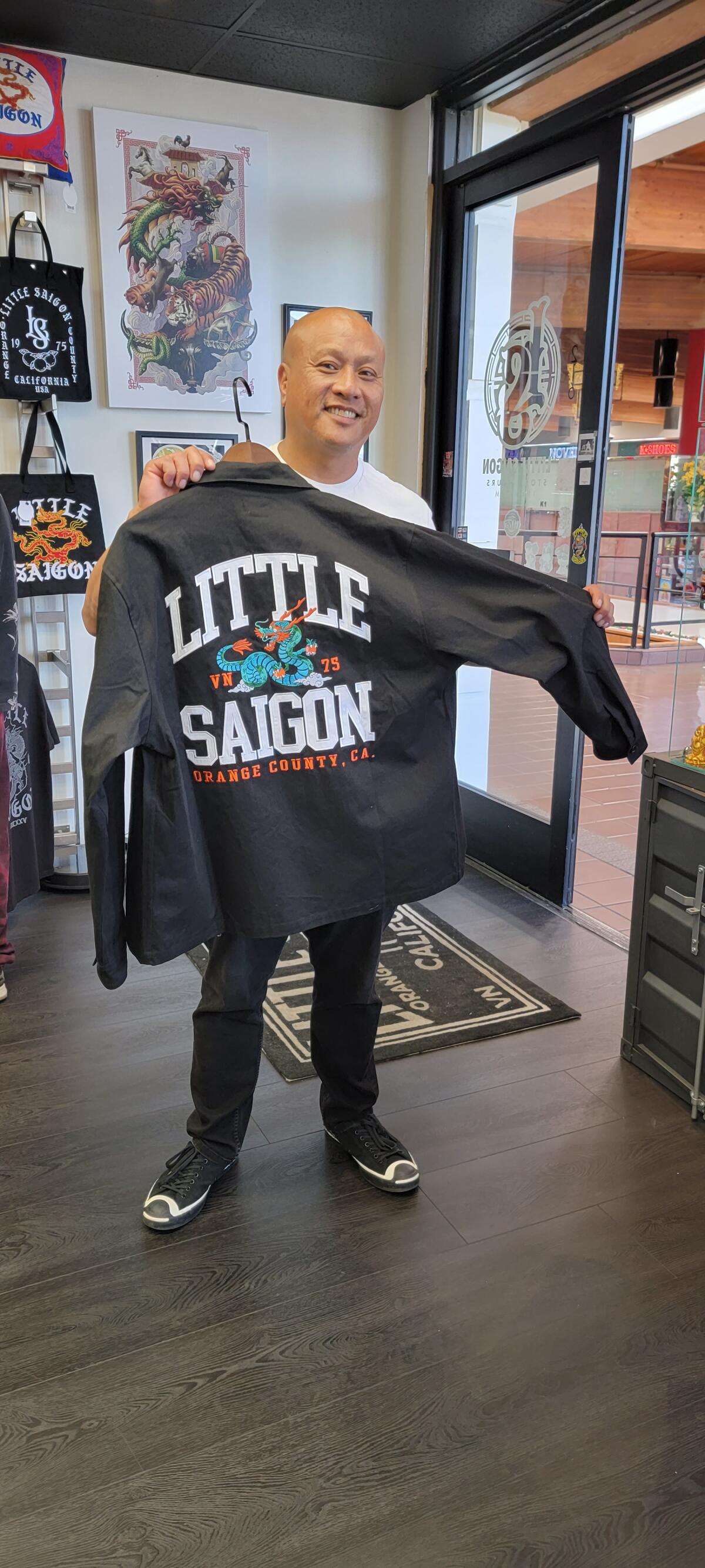 a man holds up a black sweatshirt with a drawing of a dragon holding oranges