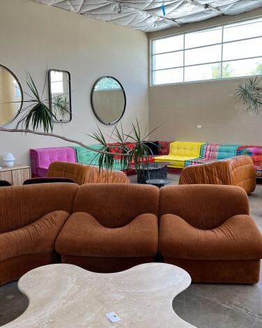 A rust-colored sectional sofa and, behind it, a multicolored sectional sofa under mirrors on the wall