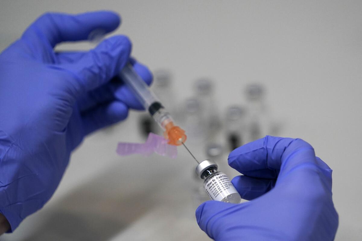 A pharmacy technician loads a syringe with Pfizer's COVID-19 vaccine.