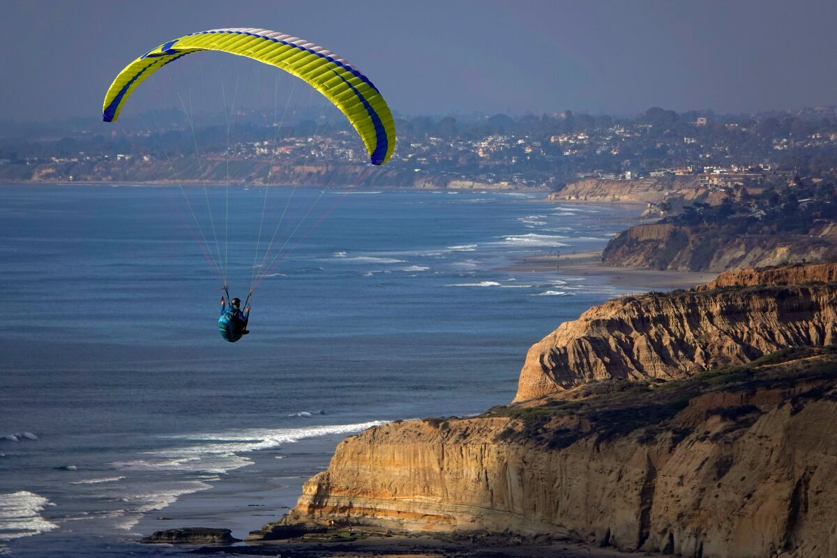 A person on a paraglider soars over the cliffs of San Diego and the Pacific Ocean.