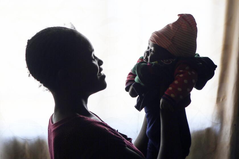 Virginia Mavhunga, a 13-year-old teenage mother, plays with her child at her rural home in Murehwa, 80 kilometres (50 miles) northeast of Zimbabwe's capital Harare, Friday, Dec. 10, 2021. Virginia dropped out of school after falling pregnant and became the subject of gossip and consternation in a community yet to adjust to the sight of a pregnant girl in school uniform. (AP Photo/Tsvangirayi Mukwazhi)