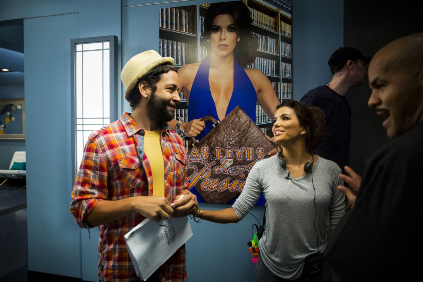 Longoria talks with actors Izzy Diaz, left, and Amaury Nolasco, right, beneath a prop poster of herself between scenes she was directing.