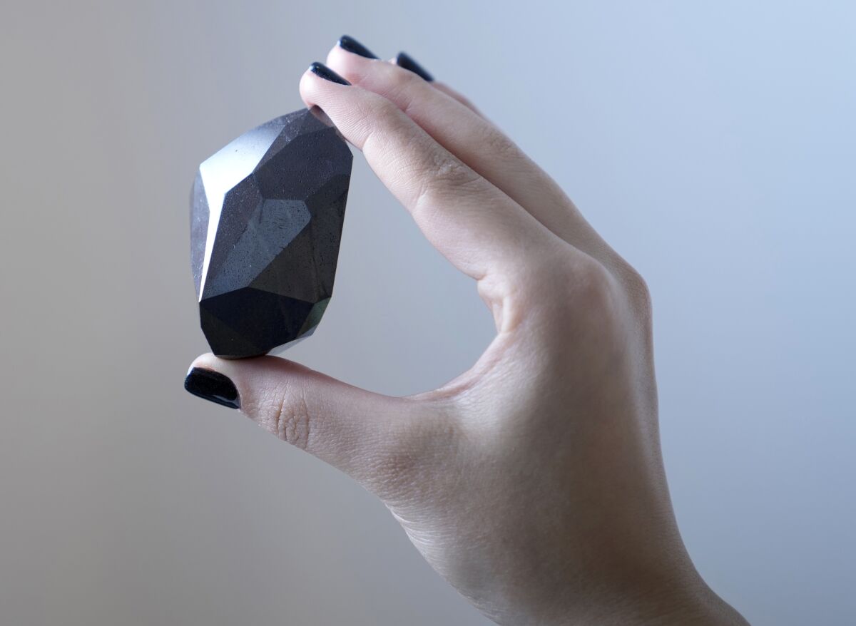 An employee of Sotheby's Dubai holds a 555.55 carat black diamond called "The Enigma" 