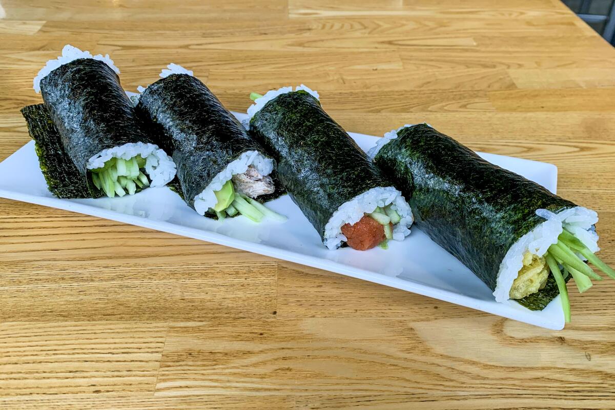 A rectangular white plate with four seaweed-wrapped hand rolls