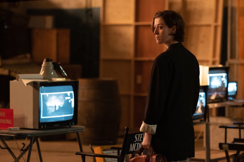 A woman stands in a room with several lit computer monitors.