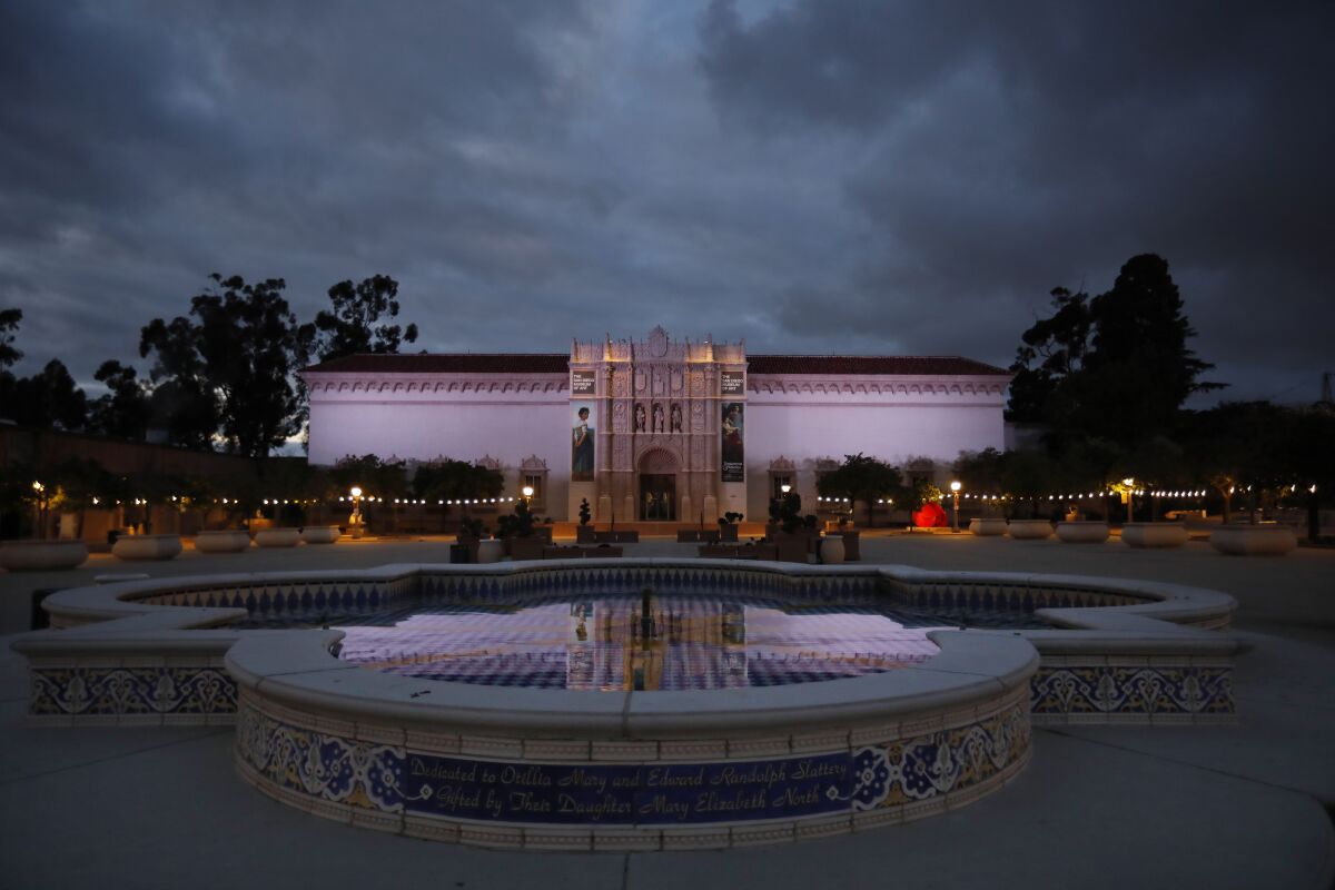 The facade of the San Diego Museum of Art reflected in a fountain, under a sky filled with dark clouds