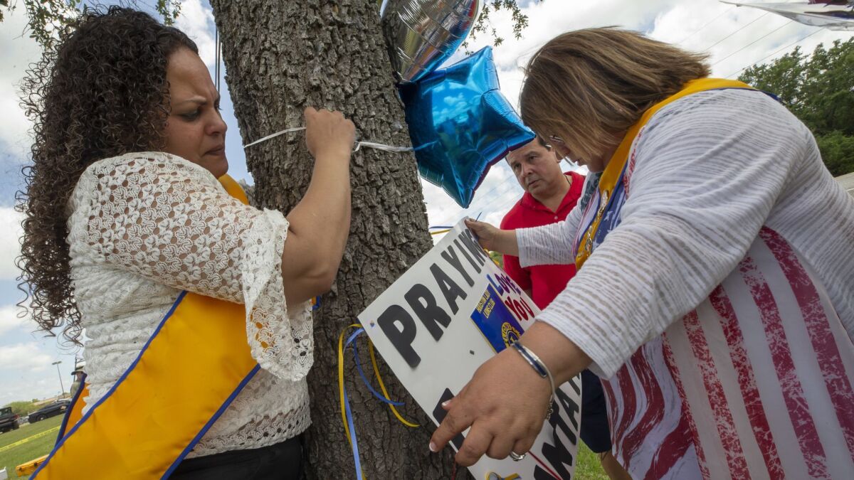 Tanya Diaz, Brock Sanchez and Lucy Gonzales place flowers, a sign and balloons on a tree outside Santa Fe High School.