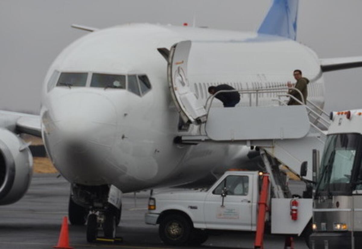 An unidentified detainee, right, in handcuffs locked to a belt chain, manages to wave to activists as he boards a U.S. Immigration and Customs Enforcement flight in Yakima, Wash.