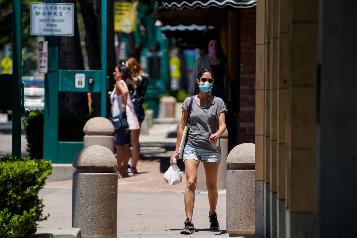 A masked woman walks along Harbor boulevard in downtown Fullerton on June 11.