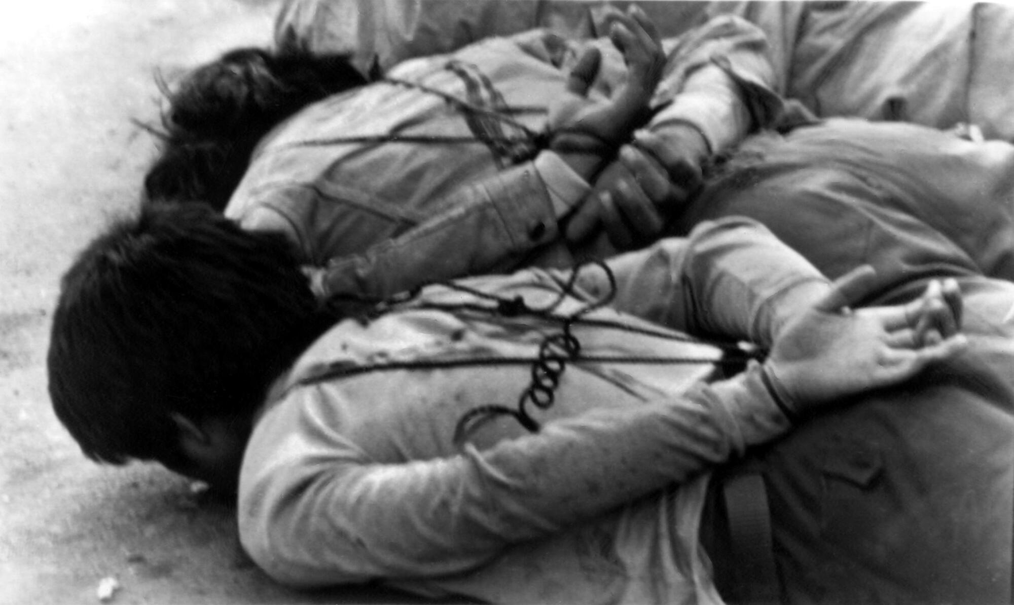 Two people lie facedown with their arms tied behind their backs