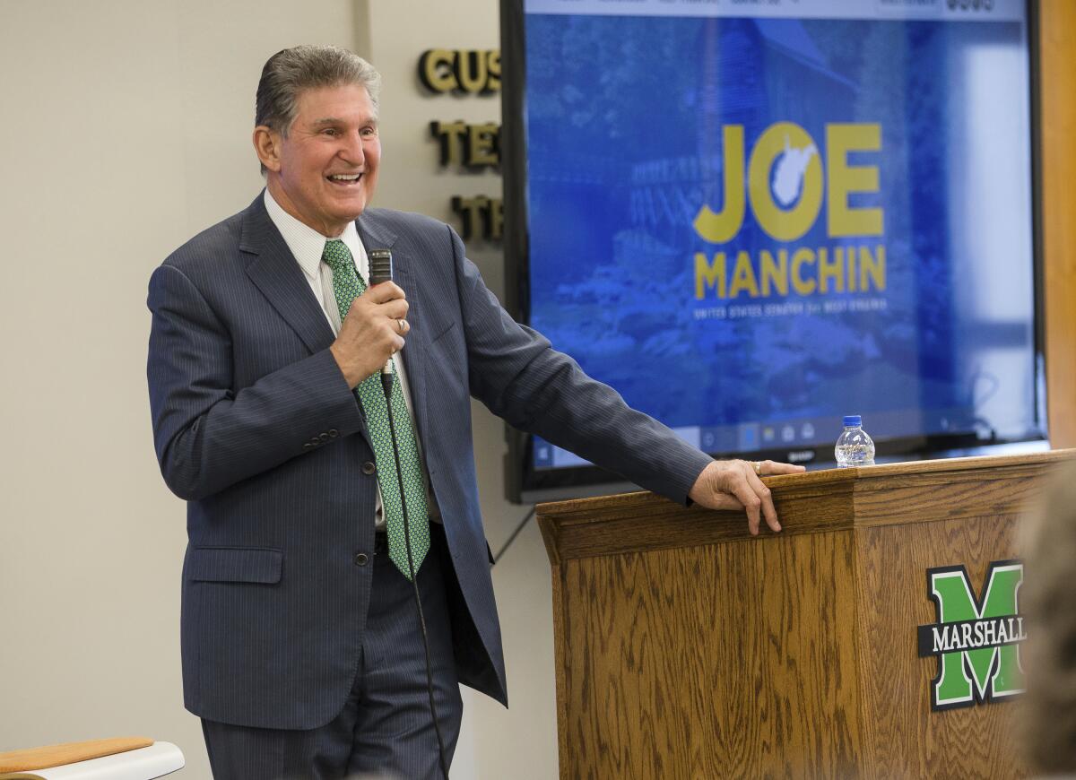 Joe Manchin, in suit and tie, smiles and speaks into a microphone.