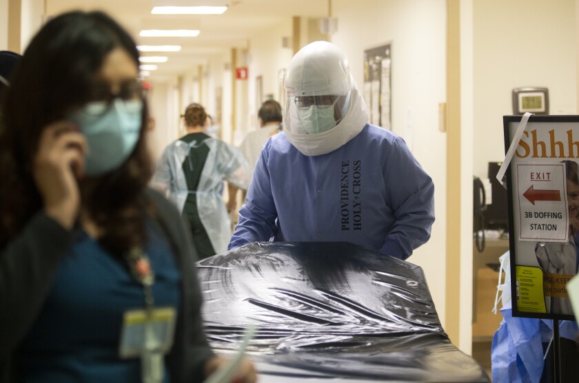 A medical worker wears a face shield and mask while pushing an object down a hospital corridor