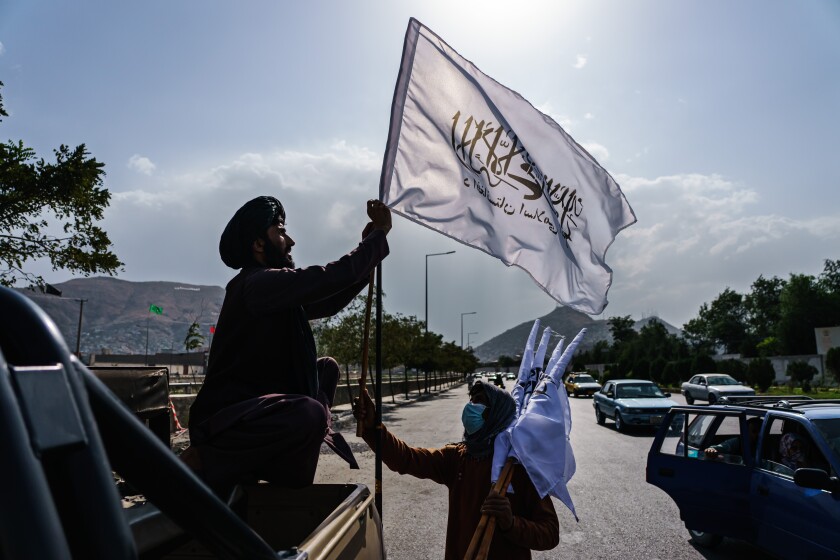 A boy with several white Taliban flags shows one to a man in a military vehicle