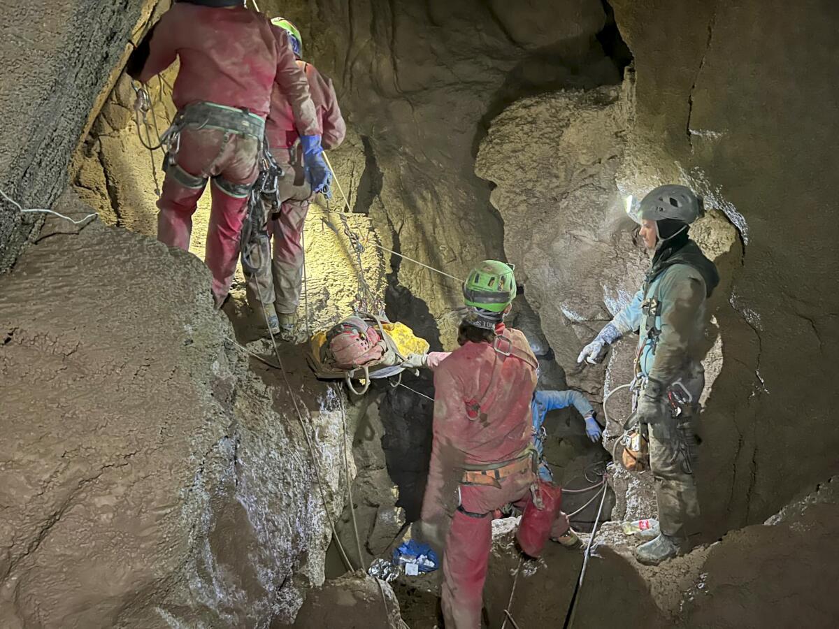 Rescuers in helmets and harnesses move a man on a stretcher through a cave. 