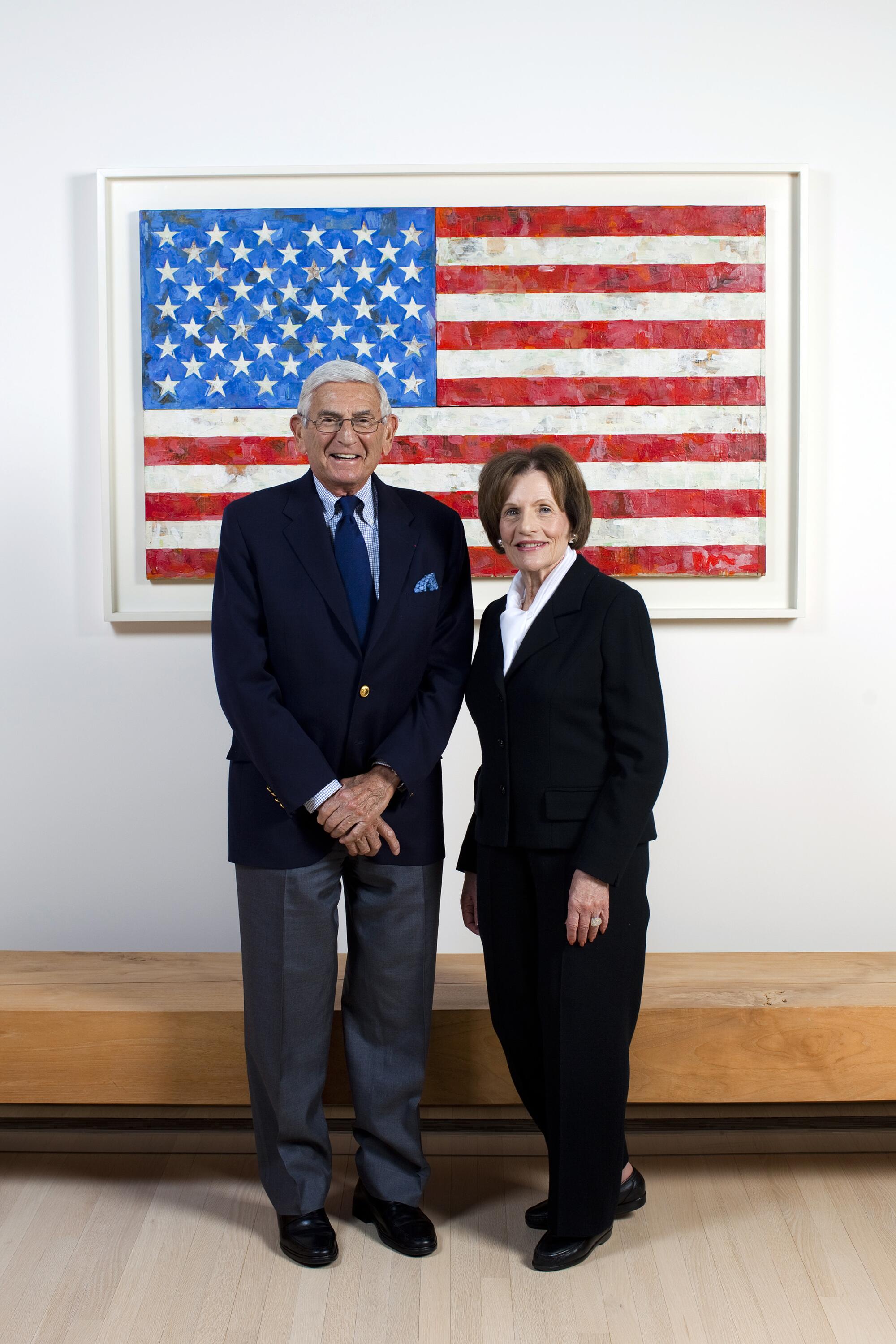 Eli and Edythe Broad pose in front of an artwork of an American flag.