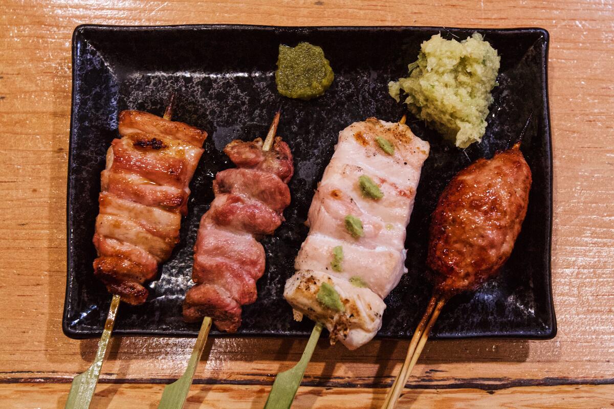 Four yakitori chicken skewers on a rectangular black plate