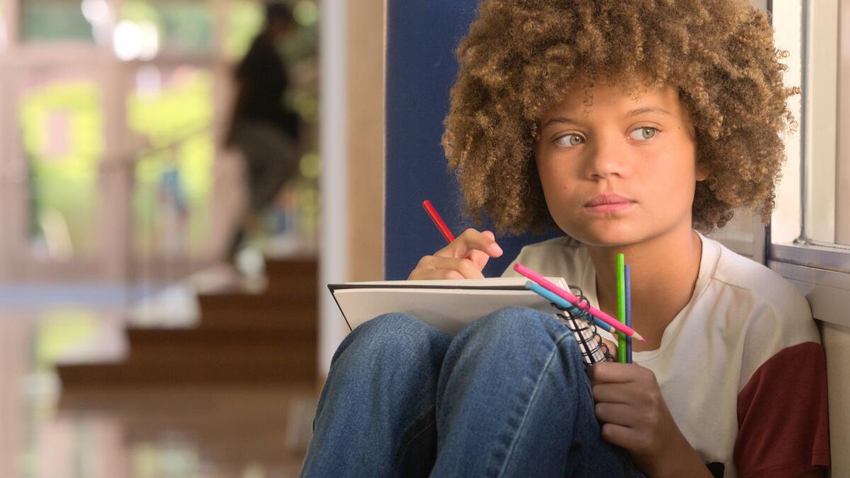 A young girl looks out the window while drawing with colored pencils on a notepad