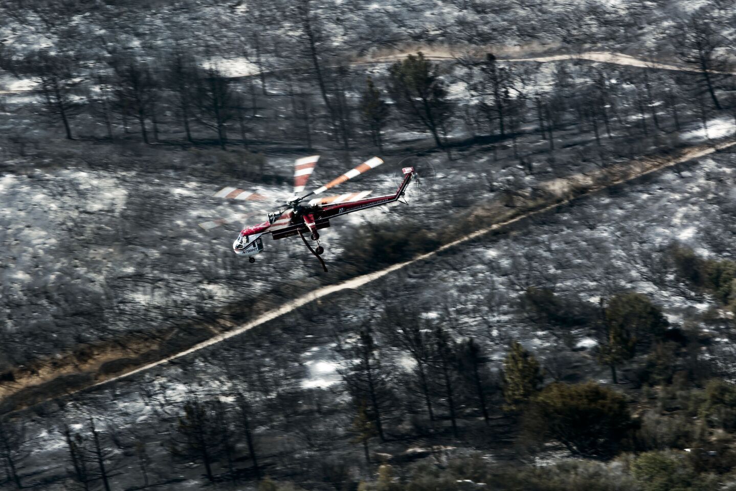 A water-dropping helicopter flies past burn areas while refueling to control the Powerhouse fire.
