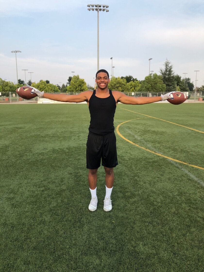 Arlis Boardingham holds his arms out with a football in each hand.