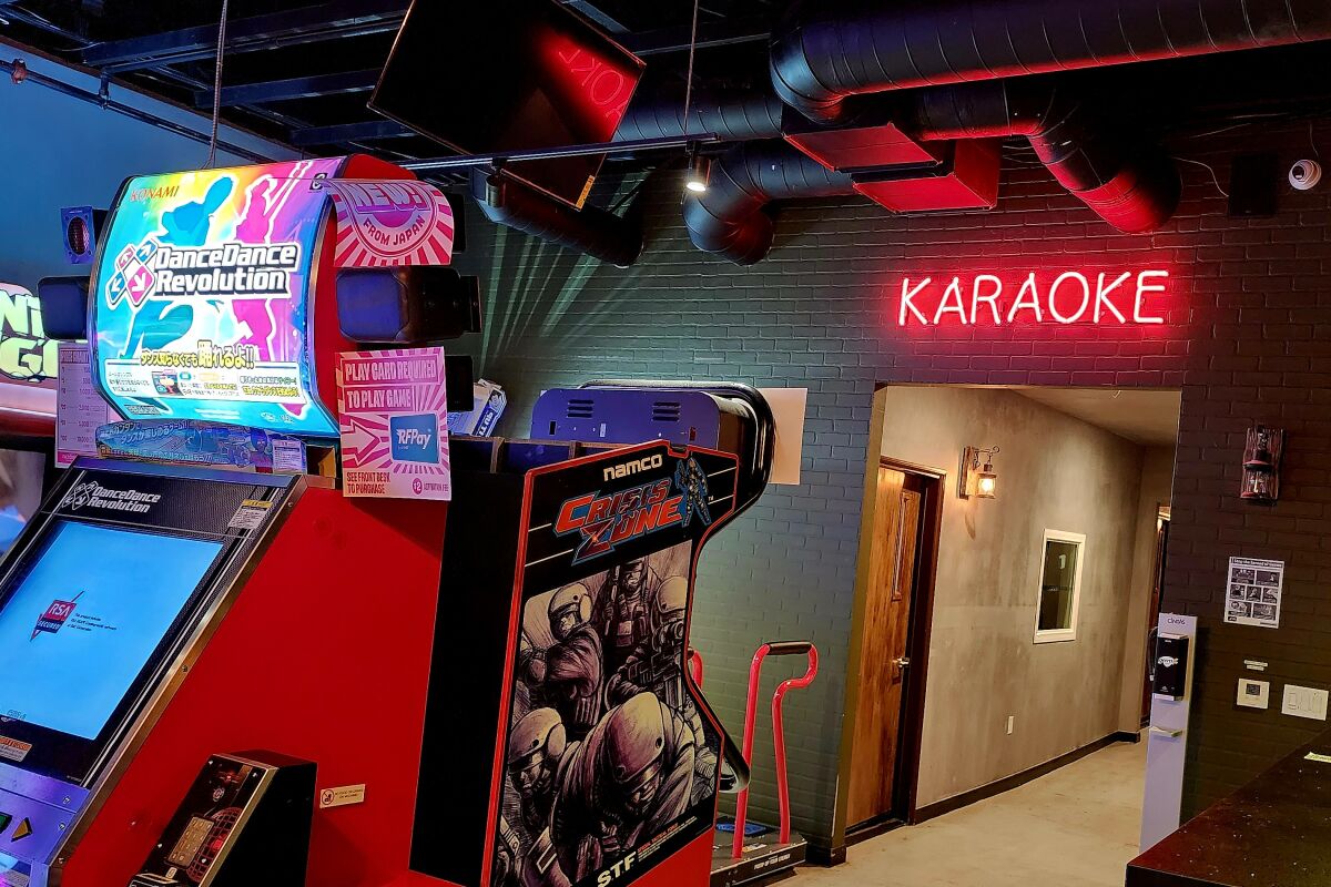 A Dance Dance Revolution machine and other arcade games at Factory Tea Bar, with a neon sign that says "karaoke"