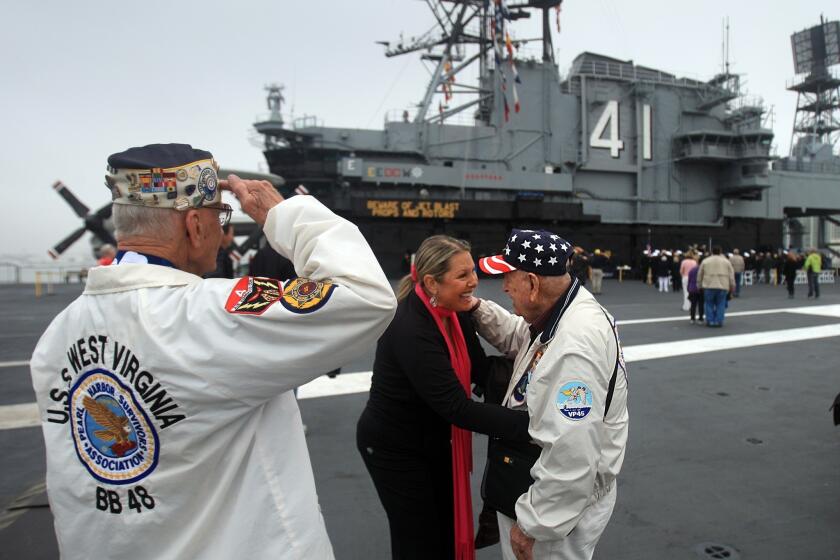 Pearl Harbor survivor Stu Hedley, 91, left, salutes, as Doyle McKee is thanked for his service by Rebecca Shaffner during the annual Pearl Harbor Day Remembrance Ceremony aboard the USS Midway Museum's flight deck in San Diego.